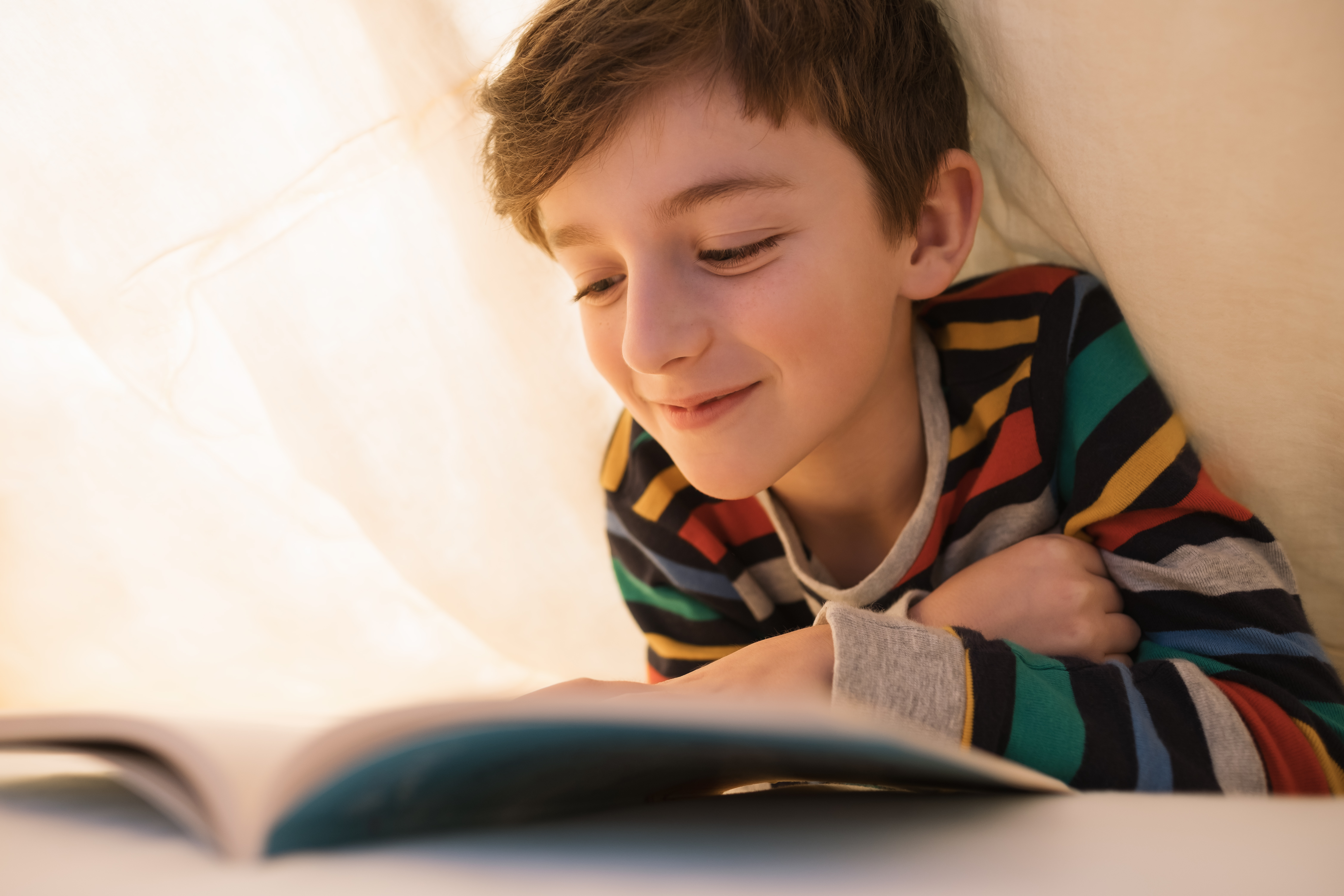 Kid reading under sheet covers in bed